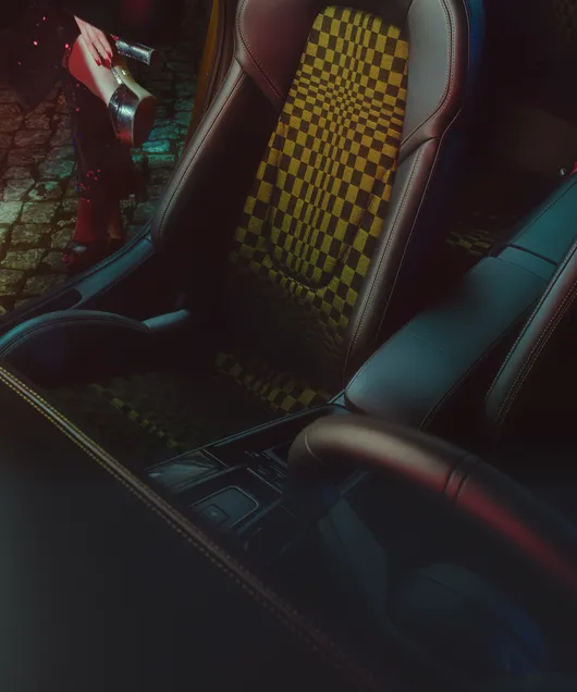 View of the passenger seat with Pasha pattern in the Porsche 911 Spirit 70. A woman's legs wearing gold platform shoes can be seen in the background.