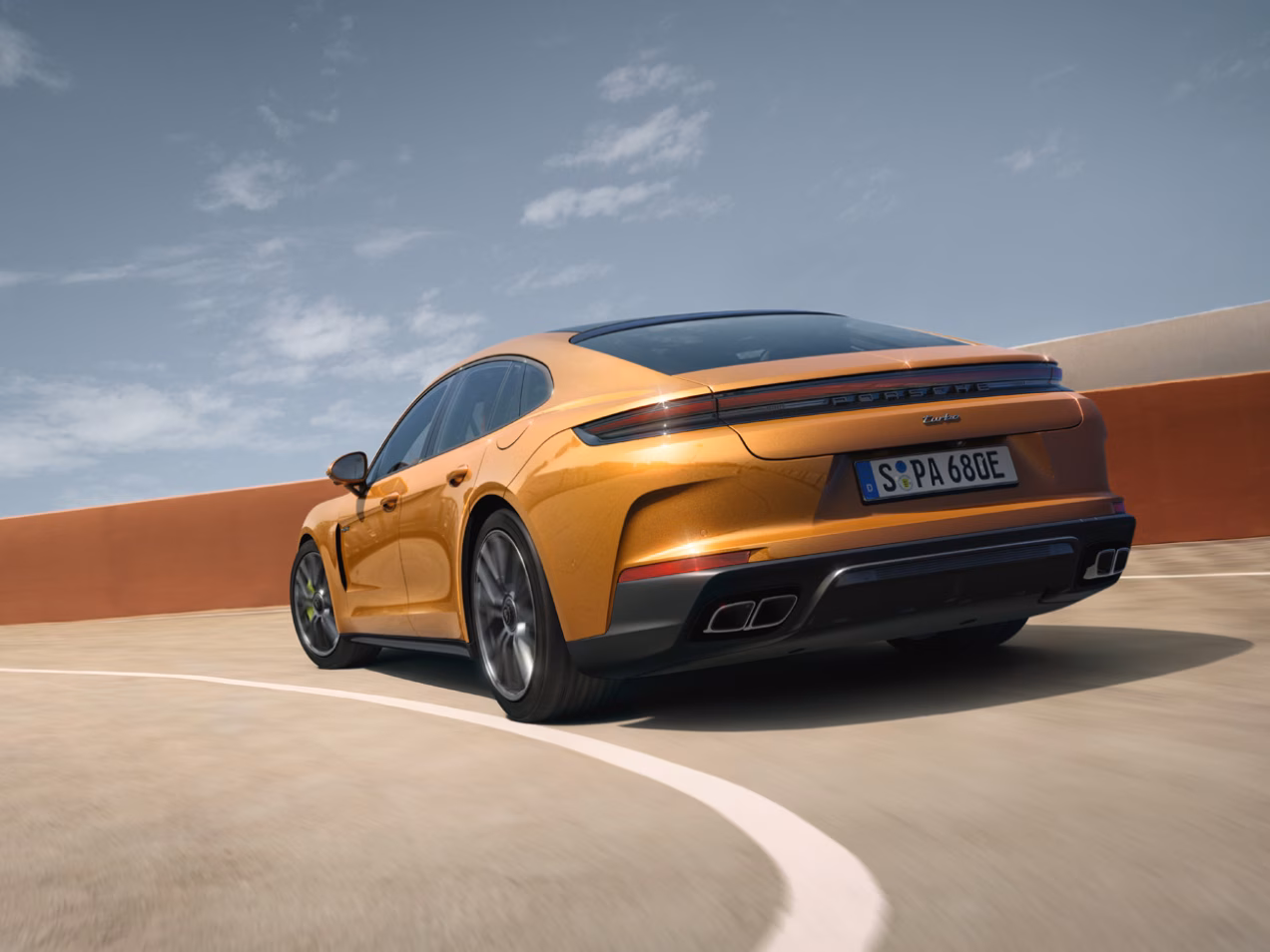 Porsche Panamera Turbo E-Hybrid in Madeira Gold Metallic navigating a bend. Rear and side view from behind.