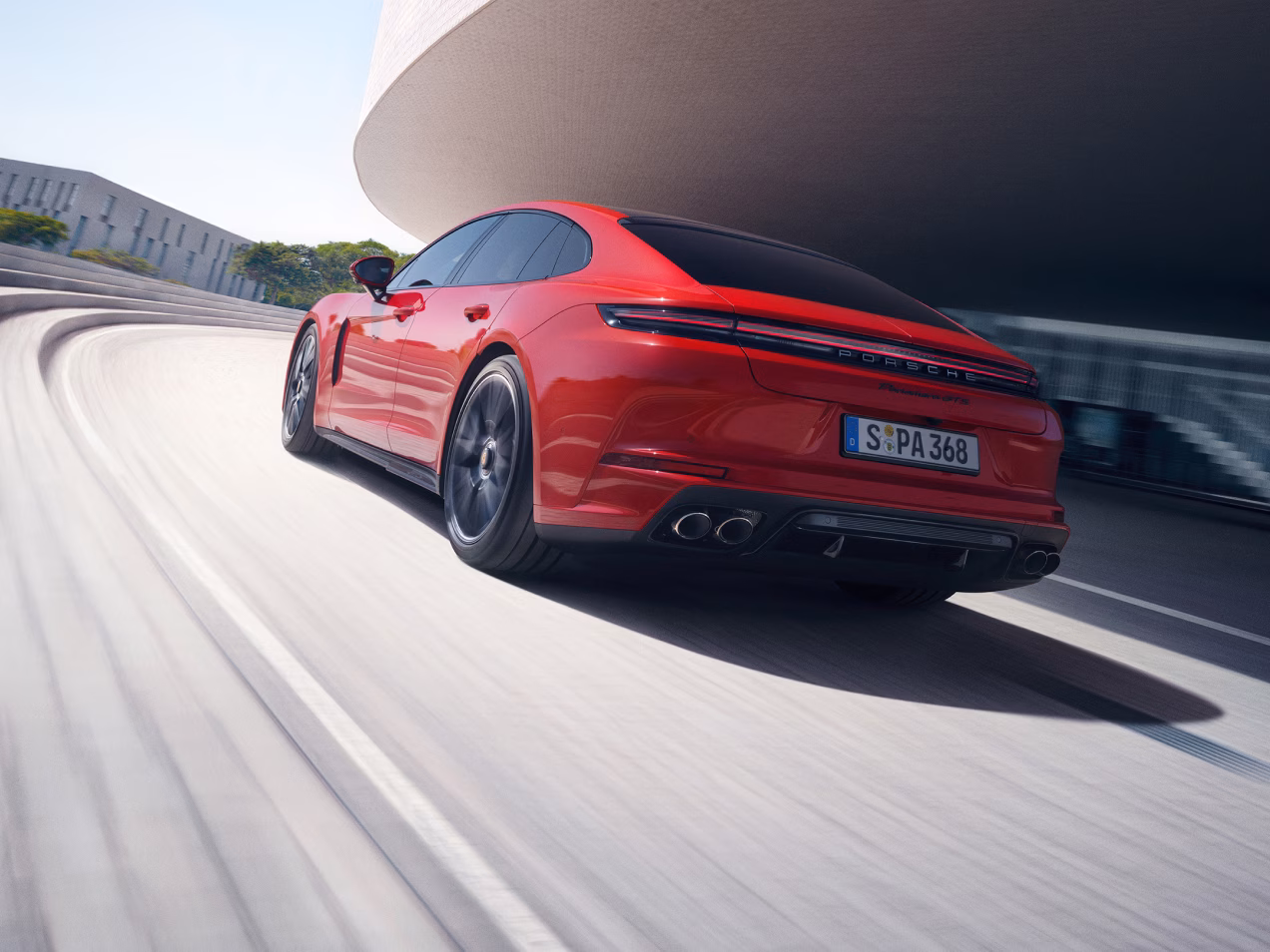 Porsche Panamera GTS in Carmine Red on a street. View of the side and rear end from behind.