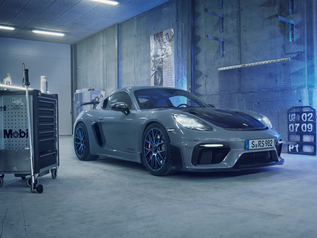 Porsche 718 Cayman GT4 RS in Arctic Grey with Weissach Package in a garage. Front and side views.