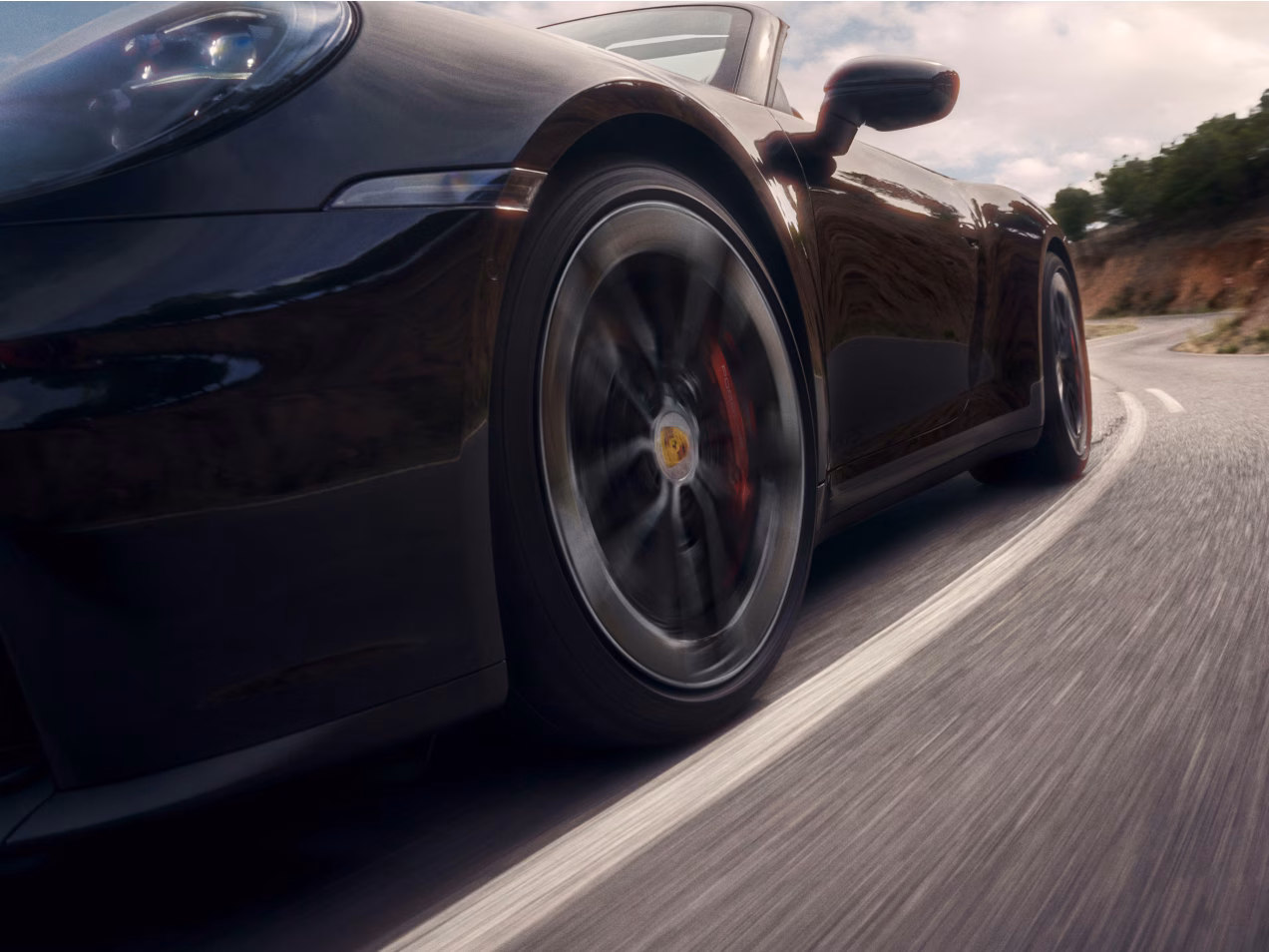 Porsche 911 Carrera GTS Cabriolet in Black driving on a road. Side view from the front.