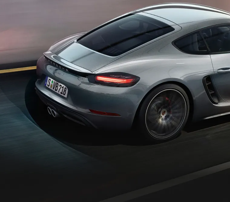 Porsche 718 Cayman S in GT Silver Metallic driving on a road. View of the rear with rear wing.