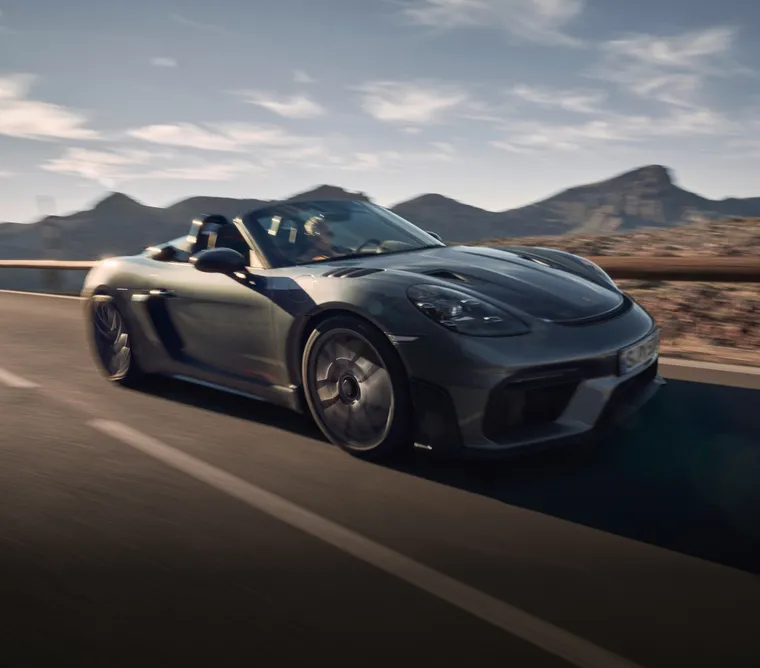 Porsche 718 Spyder RS in Vanadiumgraumetallic fährt auf Straße. Sicht auf Front und Seite.