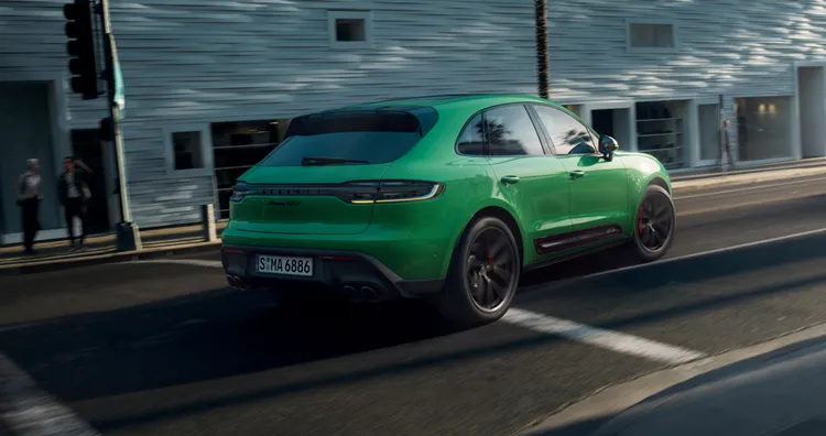 Porsche Macan GTS in Python Green driving through the city. Rear and side view.