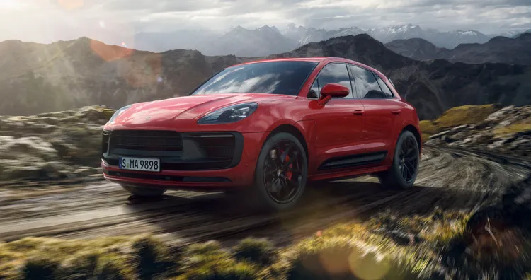 Porsche Macan GTS in Carmine Red driving through a mountain landscape. Front and side views.