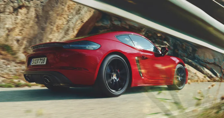 行驶在沿海公路上的胭脂红保时捷 718 Cayman GTS 4.0。低视角的后侧视图