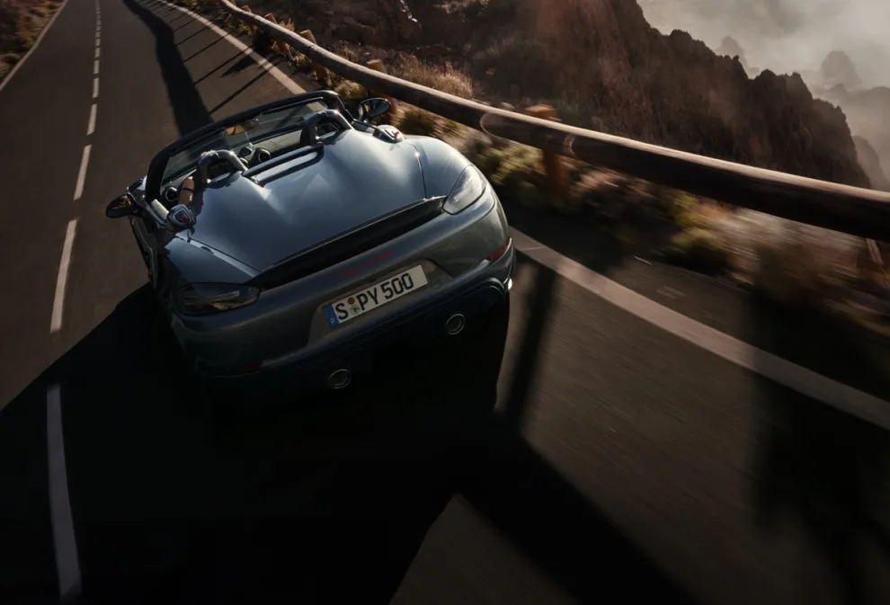 Porsche 718 Spyder RS in Vanadiumgraumetallic fährt auf Straße. Sicht von unten auf Heck und Seite.