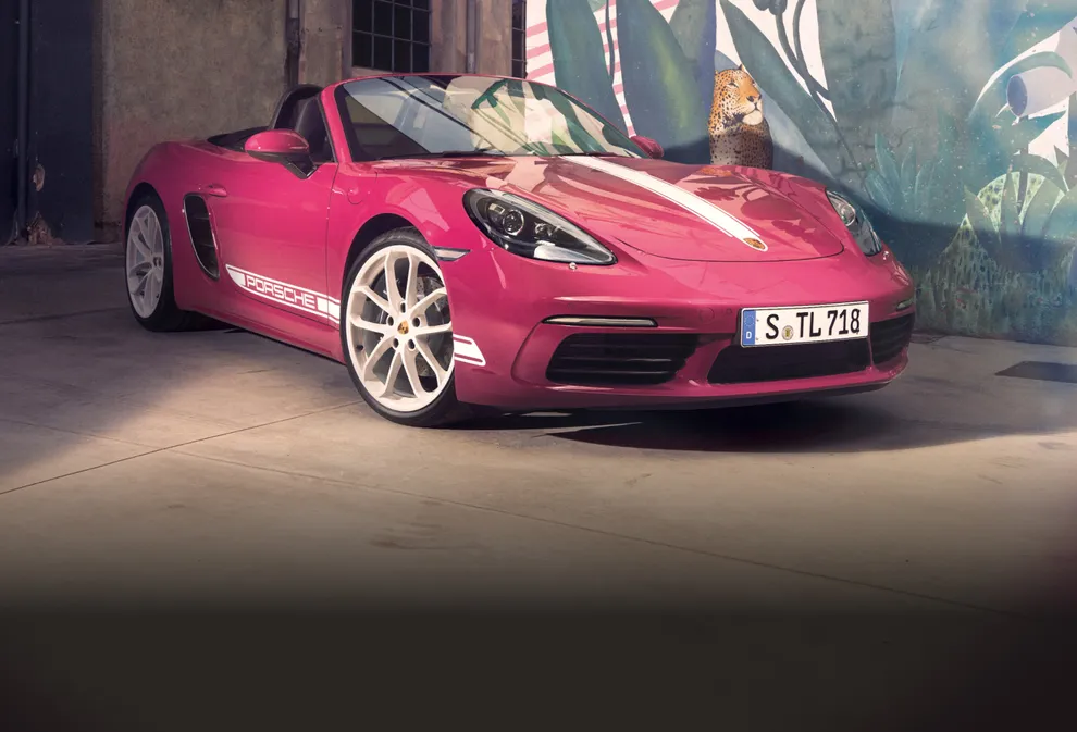 配备白色对比色组件的星光宝石红 Neo 保时捷 718 Boxster Style Edition 停在一幅壁画前前端和侧面清晰可见