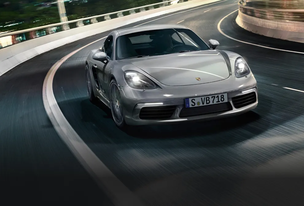 Porsche 718 Cayman S in GT Silver Metallic driving on a road. Front view.