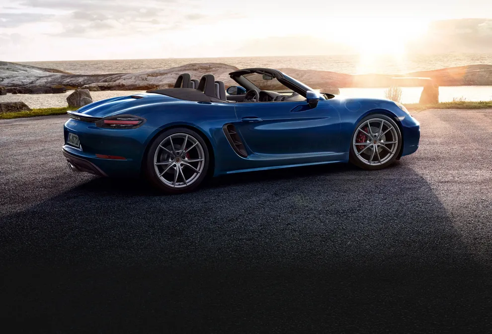 Side view of a Porsche 718 Boxster S in Gentian Blue Metallic parked in a landscape at sunset.