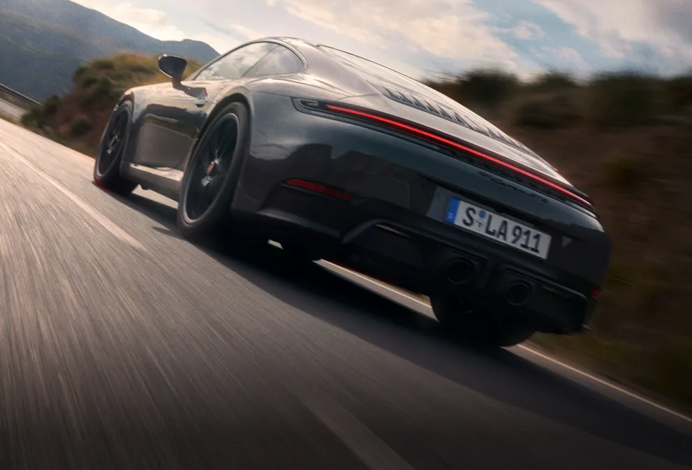 行驶在公路上的板岩灰 Neo 保时捷 911 Carrera GTS 后侧视图