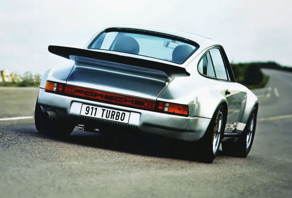 A Porsche 911 RSR Turbo is shown driving on a road from the side and behind.