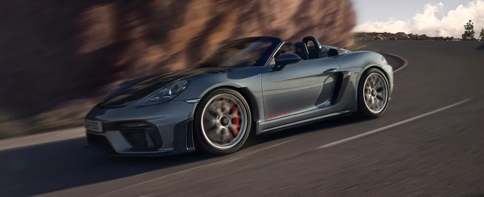 Porsche 718 Spyder RS in Vanadiumgraumetallic und ohne Verdeck fährt um Kurve. Sicht von unten auf Front und Seite.