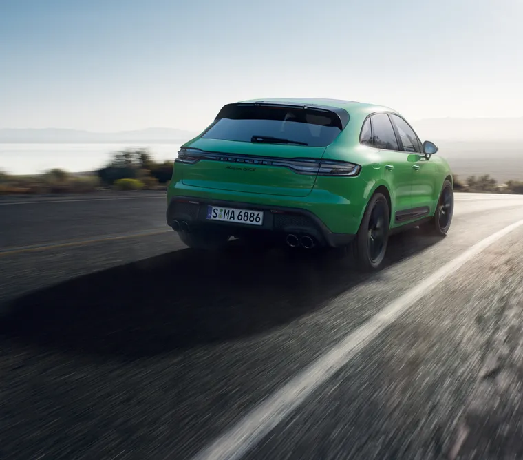 Porsche Macan GTS in Python Green driving along a country road. View of the rear end from behind.