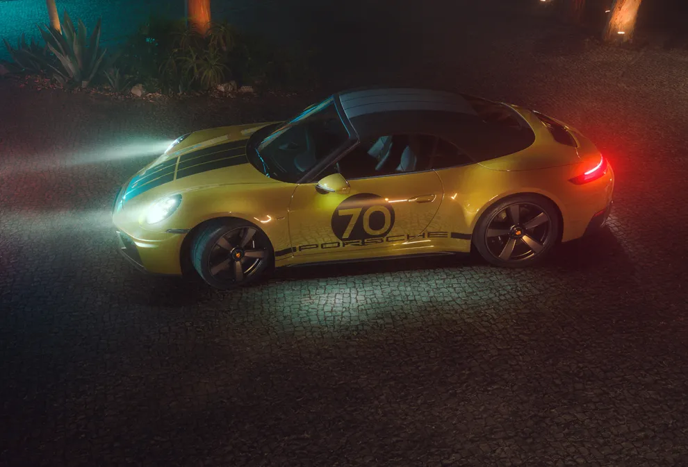 夜间，采用橄榄色 Neo 车漆的保时捷 911 Spirit 70 停在铺装广场上，车灯已开。俯瞰侧视图