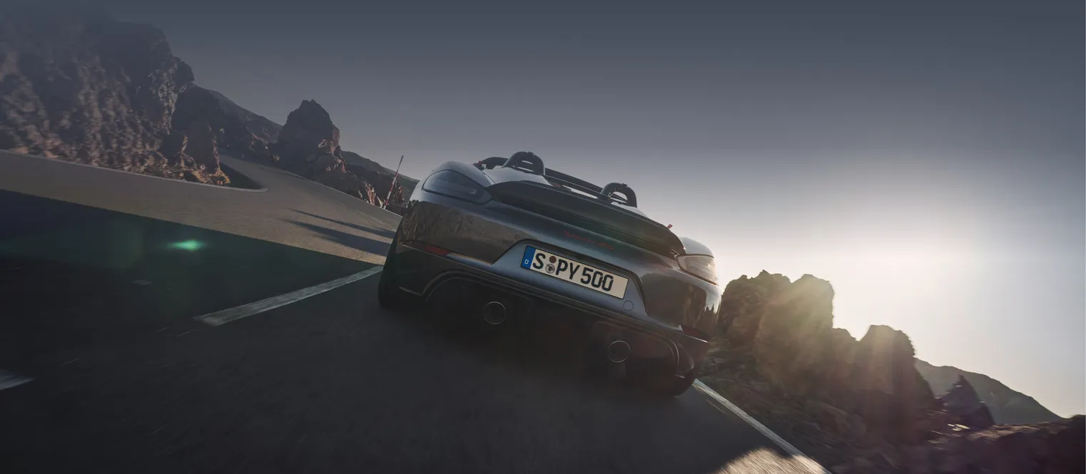 <p>Porsche 718 Spyder RS in Vanadiumgraumetallic und ohne Verdeck fährt auf Straße. Sicht von unten hinten auf das Heck.</p>