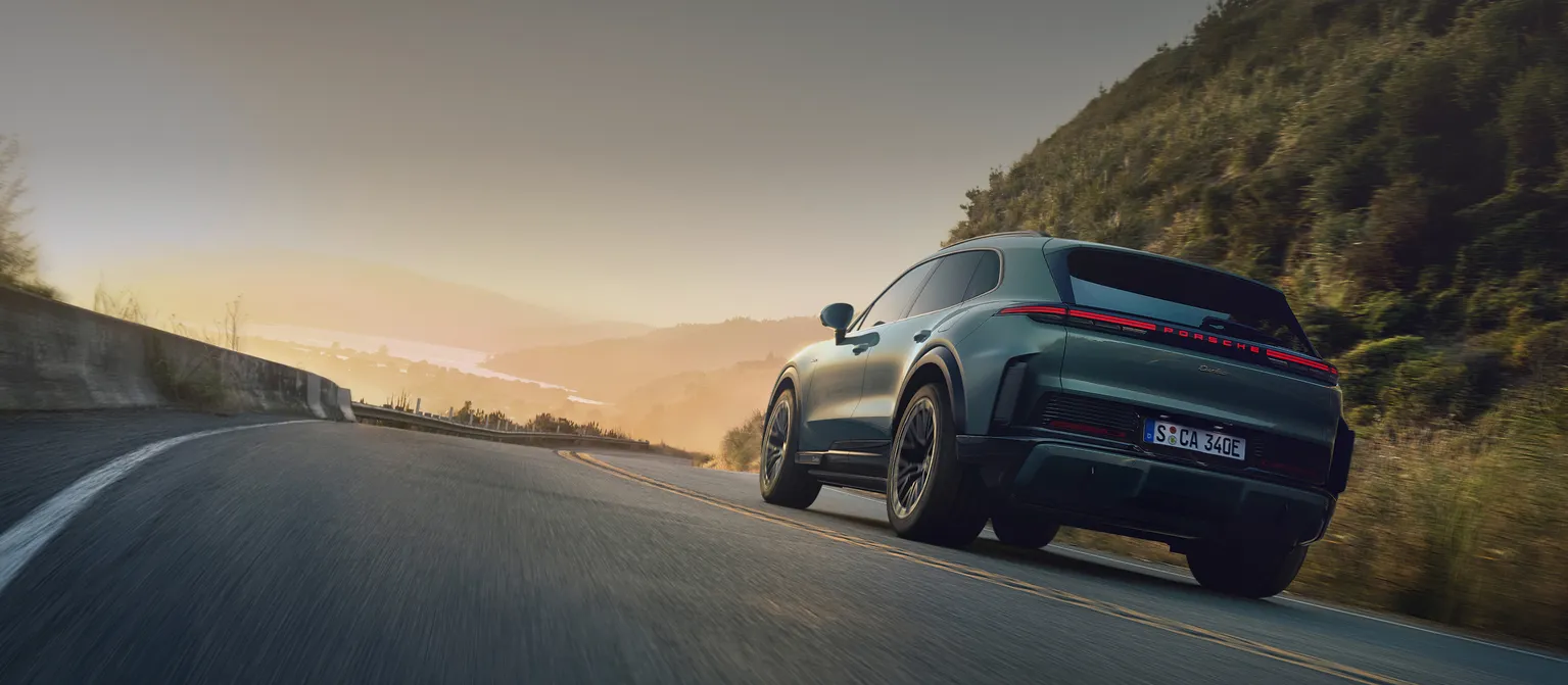 A Porsche Cayenne Turbo in Mystic Green Metallic driving on a country road. View of rear end.