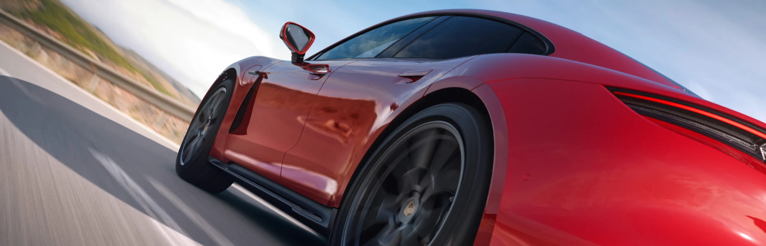 View of the rear and side of a moving Porsche Taycan GTS in Carmine Red.