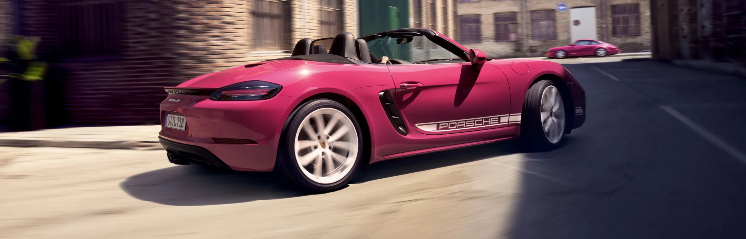 Porsche 718 Boxster in Ruby Star Neo with White Contrast Package driving through a bend. View of the side and rear.