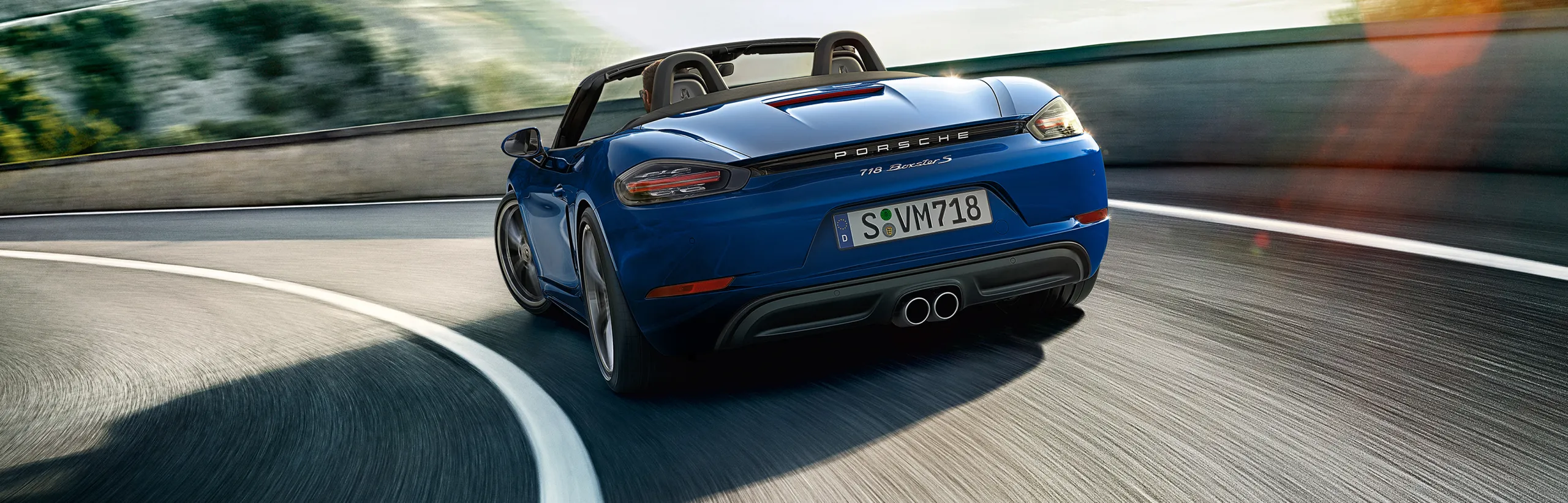 Porsche 718 Boxster S in Gentian Blue Metallic taking a bend on a mountain road. View of the rear end.