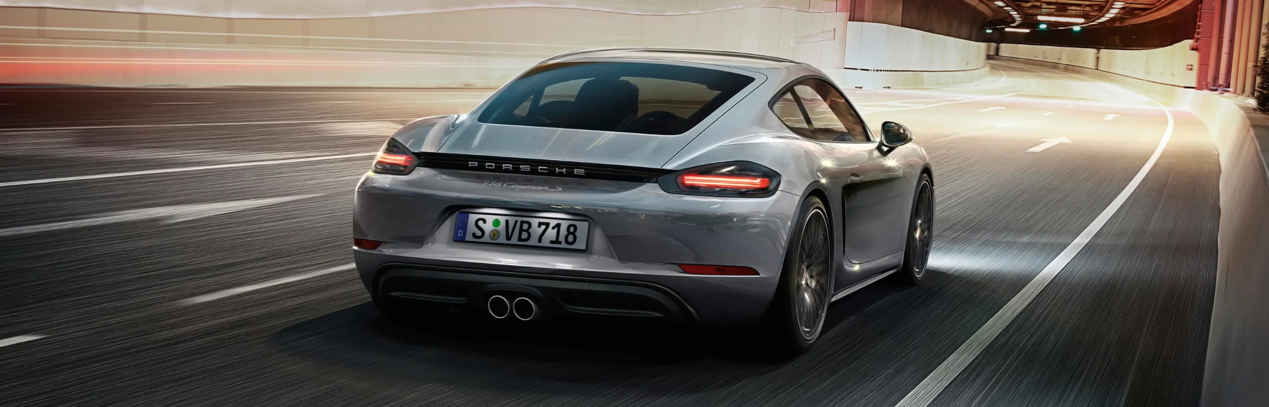 Porsche 718 Boxster S in Gentian Blue Metallic taking a bend on a mountain road. View of the rear end.