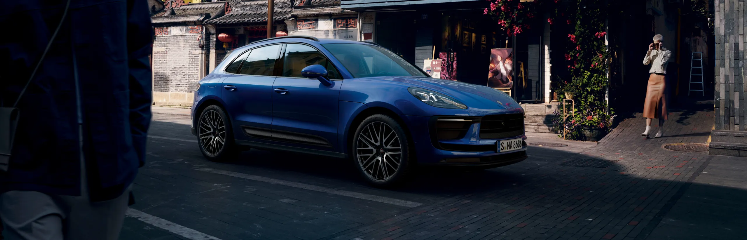 Porsche Macan in Gentian Blue Metallic on a street in front of a gallery. Side view.
