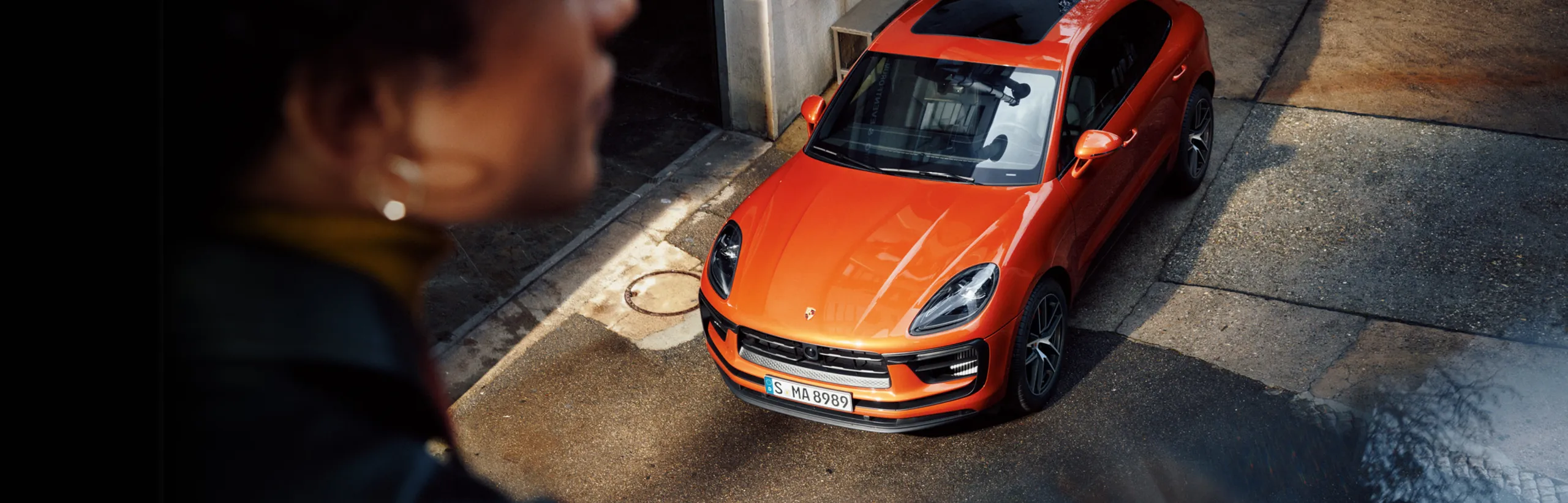 城市中的帕派雅橙金属漆保时捷 Macan S。前端和车顶俯视图