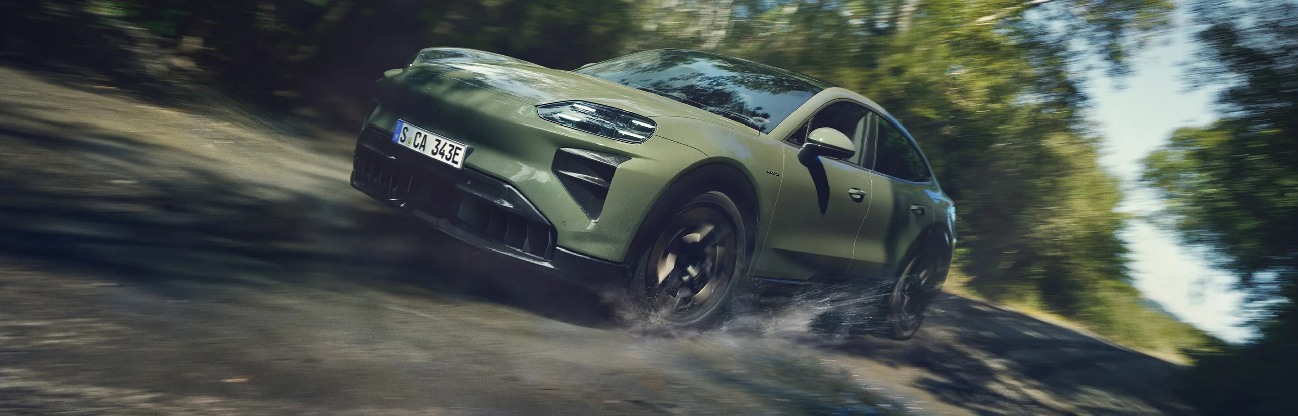 A Porsche Cayenne Turbo Coupé in Monteverde Metallic driving off-road. View of the front and side.