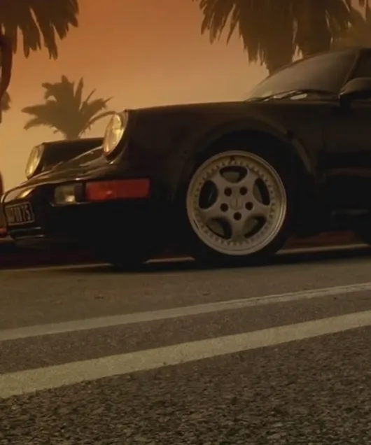 落日和棕榈树为背景下，黑色保时捷 911 Turbo 3.6 (964) 的侧面视图 