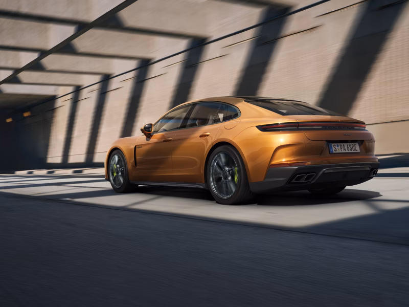 Porsche Panamera Turbo E-Hybrid in Madeira Gold Metallic navigating a bend. Rear and side view from behind.