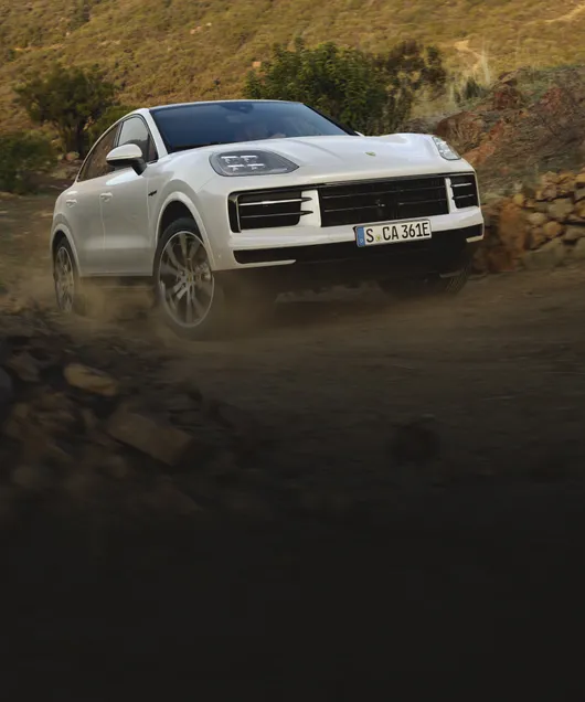 在碎石路上越野行驶的细花白金属漆新款保时捷 Cayenne E-Hybrid Coupé 插电式混合动力车型前视图 / 前裙板