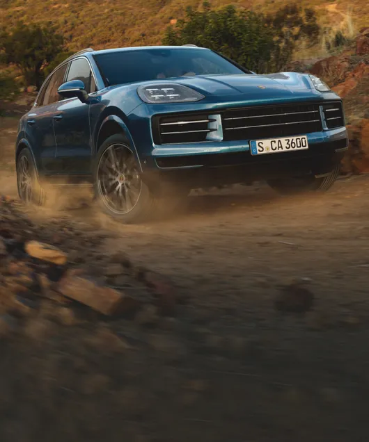 Porsche Cayenne in Montego Blue Metallic driving off-road on a gravel road. View of front / front apron.