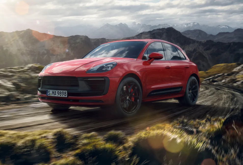 Porsche Macan GTS in Carmine Red driving through a mountain landscape. Front and side views.