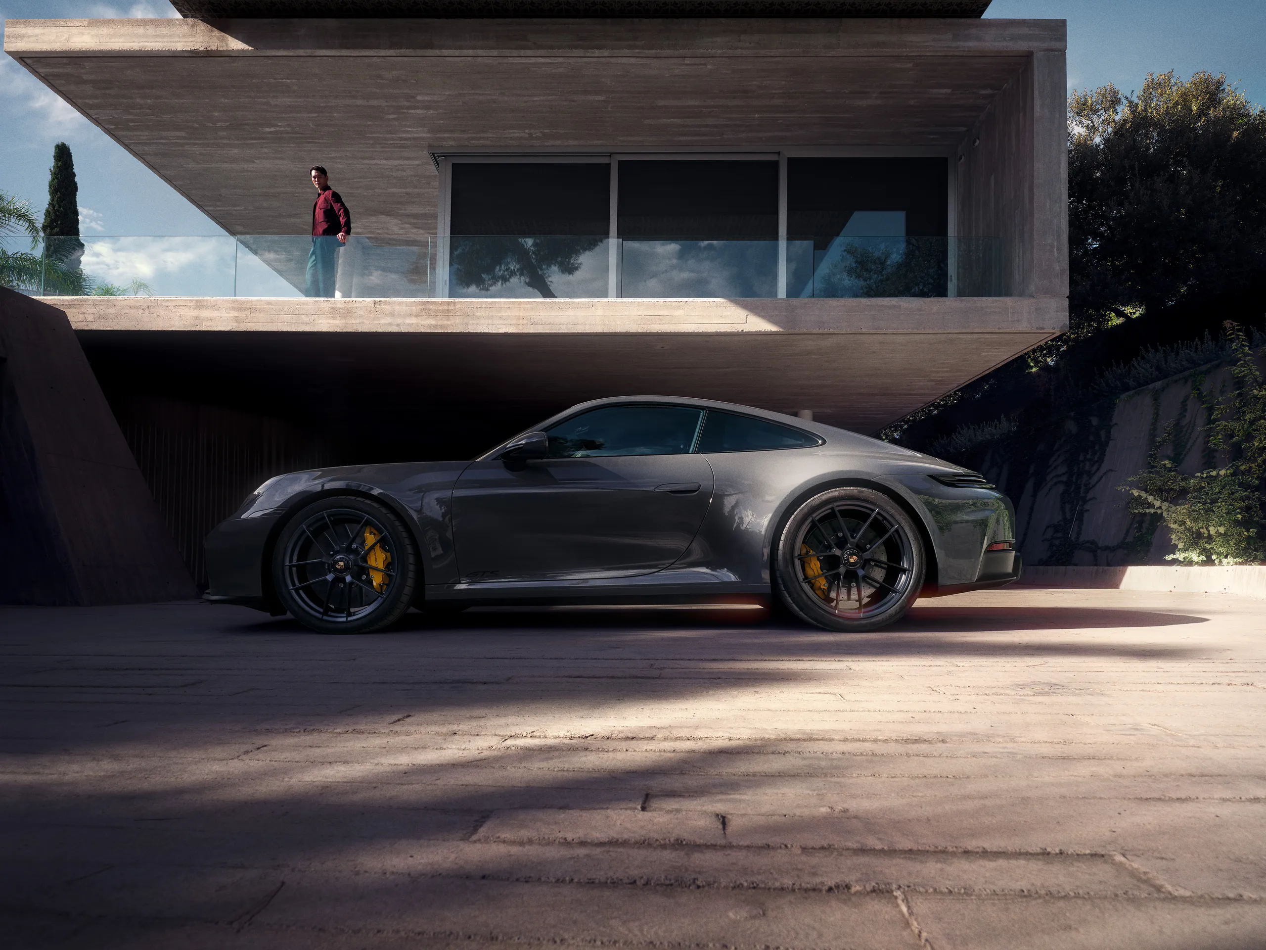 Side shot of  a Slate Grey Neo colored 911 Carrera GTS standing in front of a modern building.