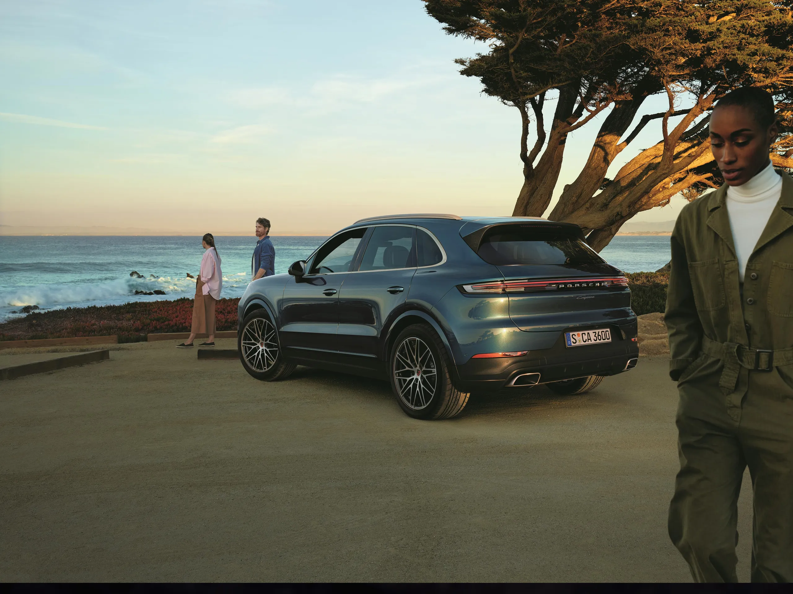 A group of people standing in front of a Cayenne on a coastline.