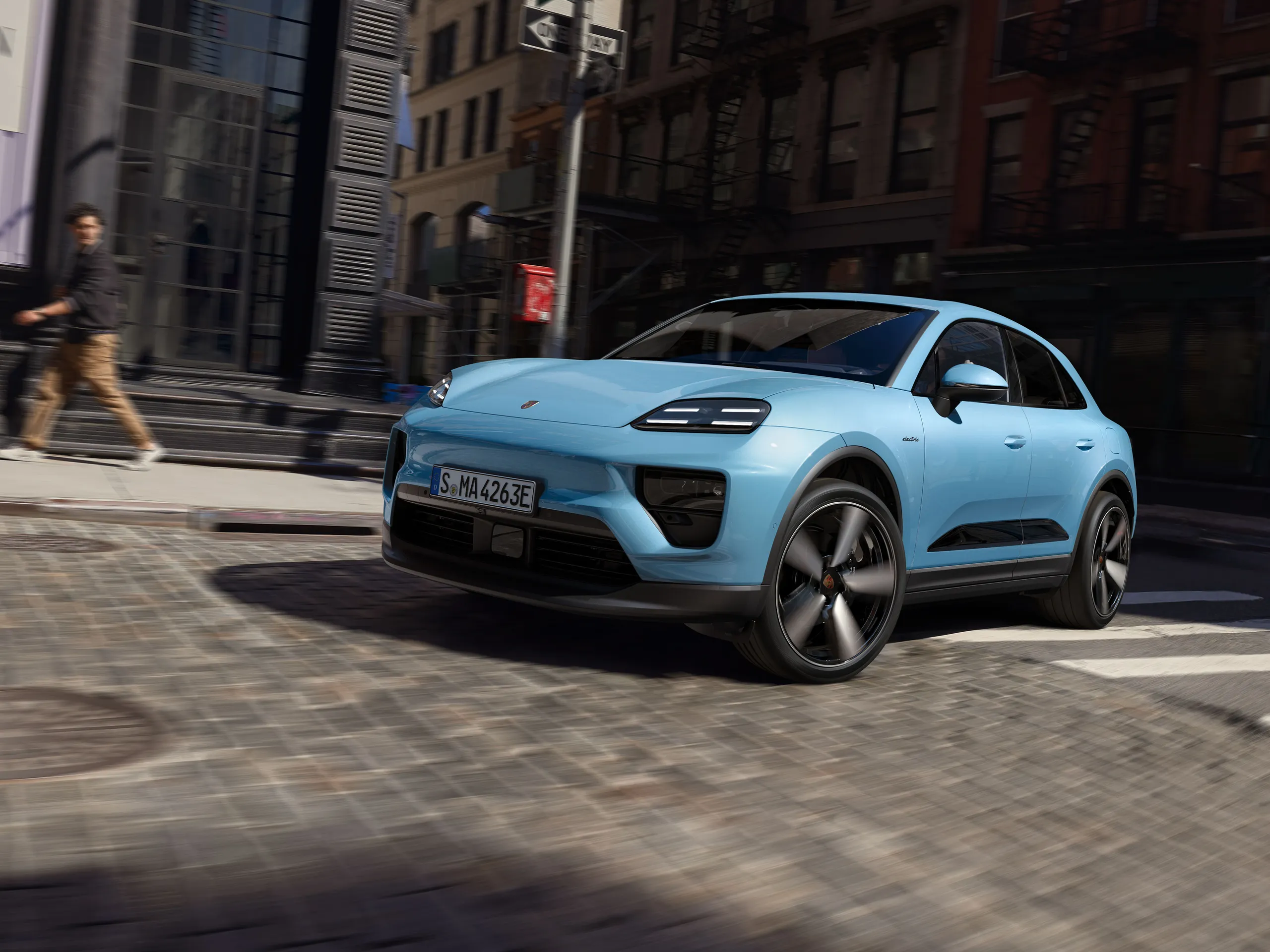 Front shot of a Frozen Blue Metallic Macan Electric driving through the city.